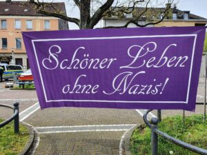 Zwischen Bäumen aufgespanntes lilanes Banner mit der Aufschrift "Schönder leben ohne Nazis"