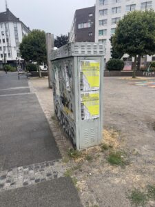 Zwei Plakate für die Demo "Scheiß Nazis. Scheiß Heimat." am 01.08., die an einen Stromkasten geklebt wurden. Im Hintergrund der Mehmet-Kubaşık-Platz in der Dortmunder Nordstadt.